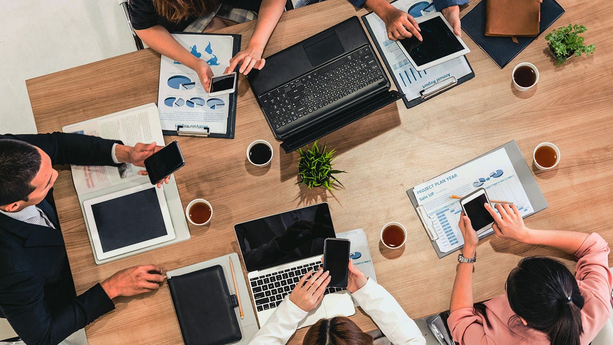 A group of coworkers meeting while using laptops, tablets, and cell phones.