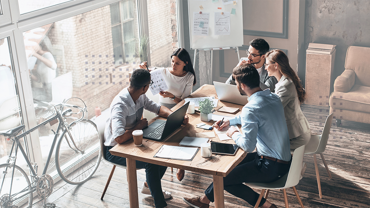 A group of employees sitting around a table collaborating with a laptop and tablet